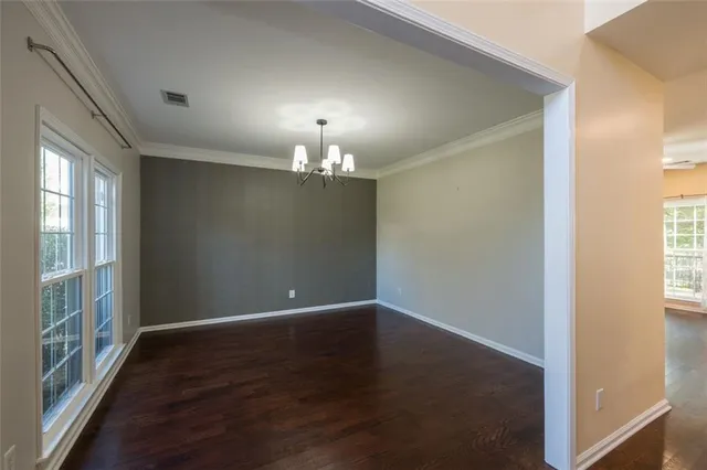 an empty room with wooden floor chandelier and windows