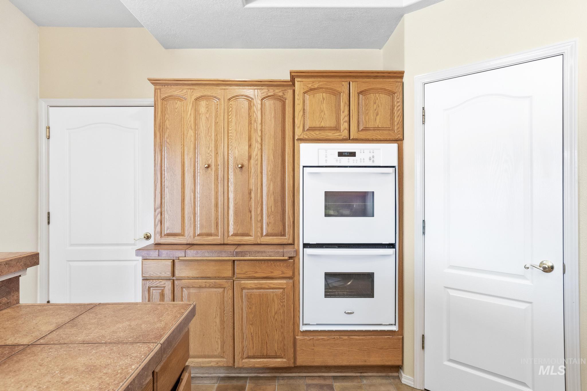 15181 Drury Way Caldwell, ID 83607 - Photo 20 of 49 Kitchen area featuring wood-finish cabinetry, integrated double wall ovens, and tiled countertops