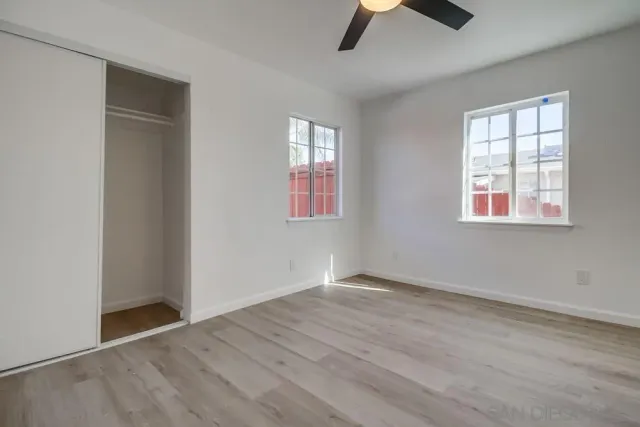 an empty room with wooden floor chandelier fan and windows