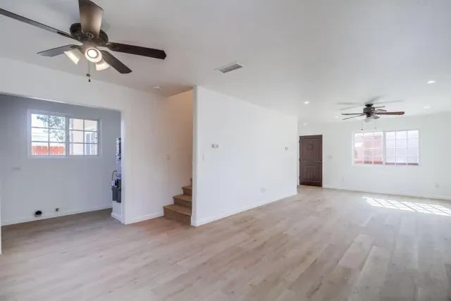 an empty room with wooden floor fan and windows