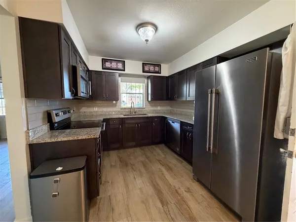 a kitchen with stainless steel appliances granite countertop a refrigerator a sink dishwasher a stove with wooden cabinets and floor
