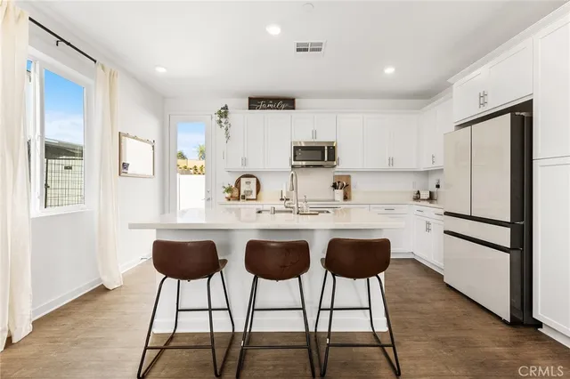 a kitchen with stainless steel appliances a stove a sink refrigerator and white cabinets with wooden floor