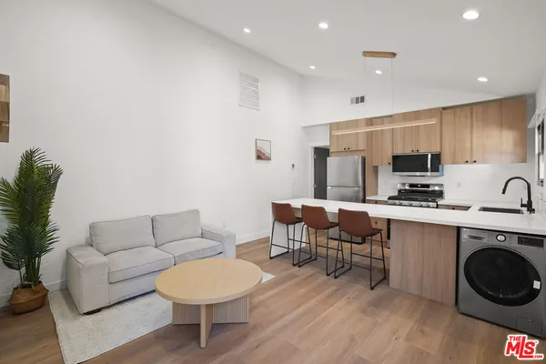 a living room with furniture a kitchen island with wooden cabinets and stainless steel appliances