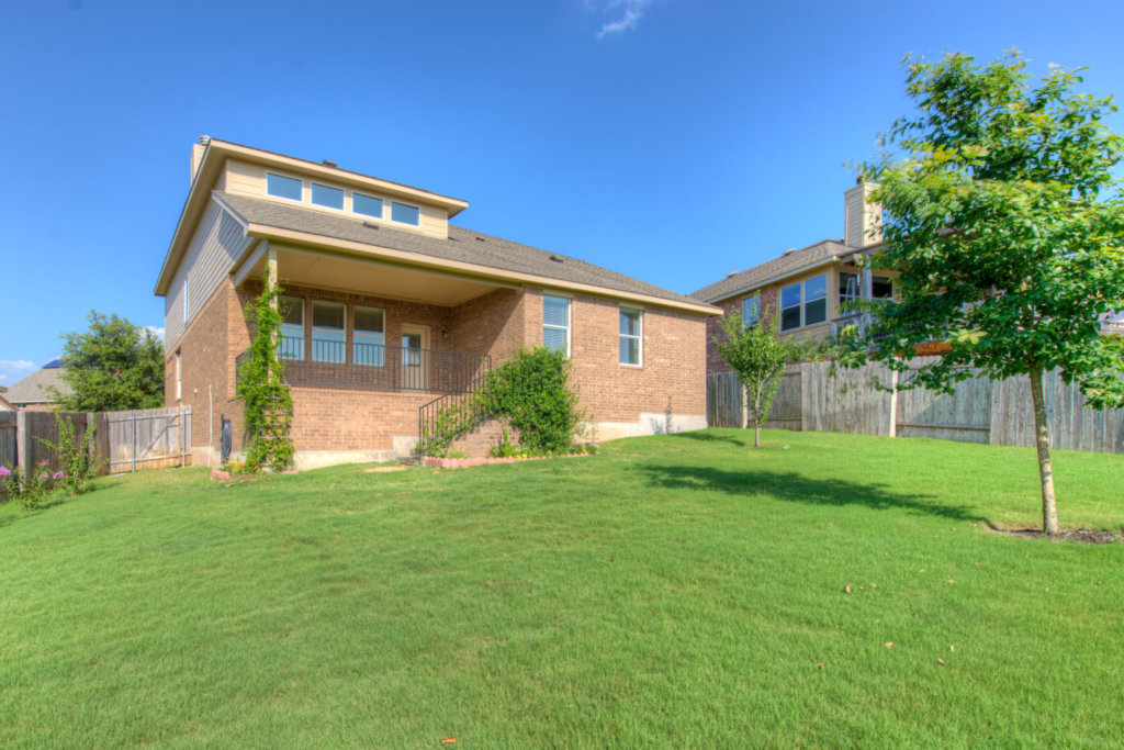 403 Limestone Trail Austin, TX 78737 - Photo 18 of 18 A fenced backyard offers a private retreat with mature trees and a brick-built home featuring an elevated porch.