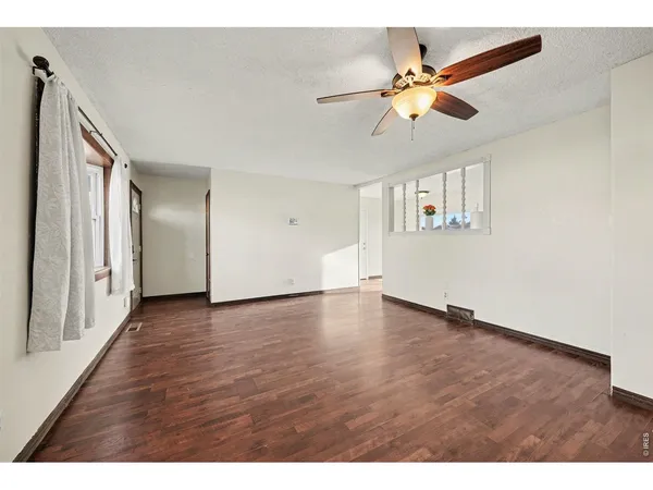 a view of an empty room with wooden floor and a ceiling fan