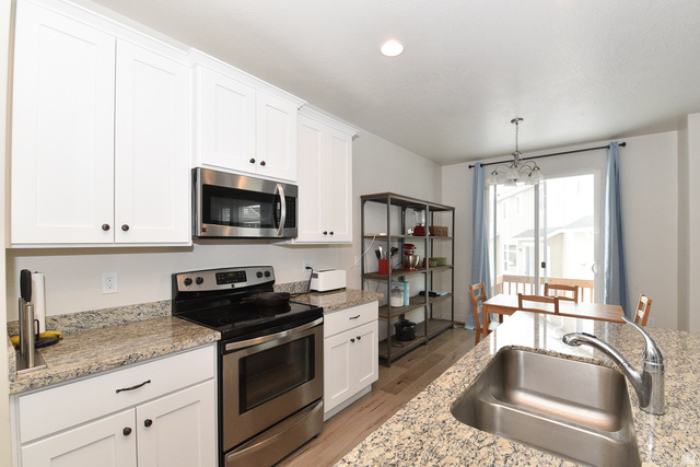 1632 North Apache Road Saratoga Springs, UT 84045 - Photo 6 of 28 Kitchen featuring white cabinetry, stainless steel appliances, granite countertops, wood-finish flooring, and a sliding glass door