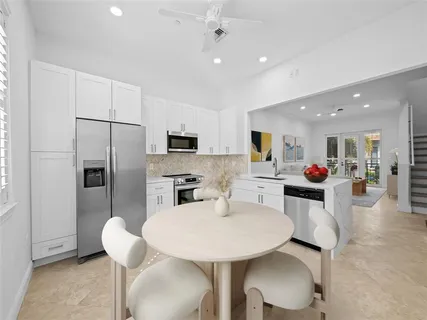 a kitchen with stainless steel appliances a dining table chairs refrigerator and sink
