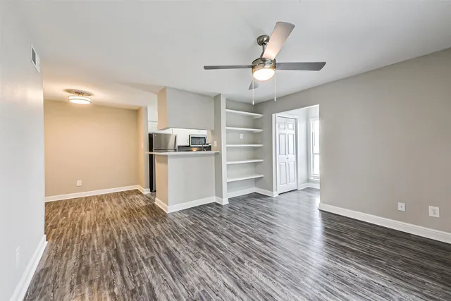 a view of an empty room with wooden floor and a ceiling fan