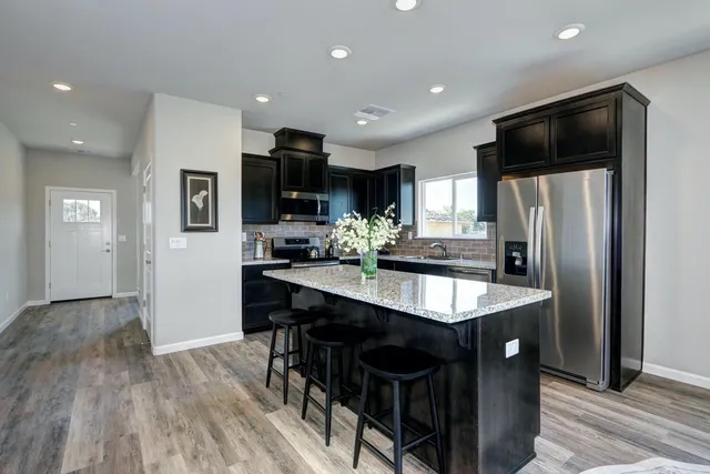 a kitchen with stainless steel appliances granite countertop a refrigerator a stove a sink a dining table and chairs