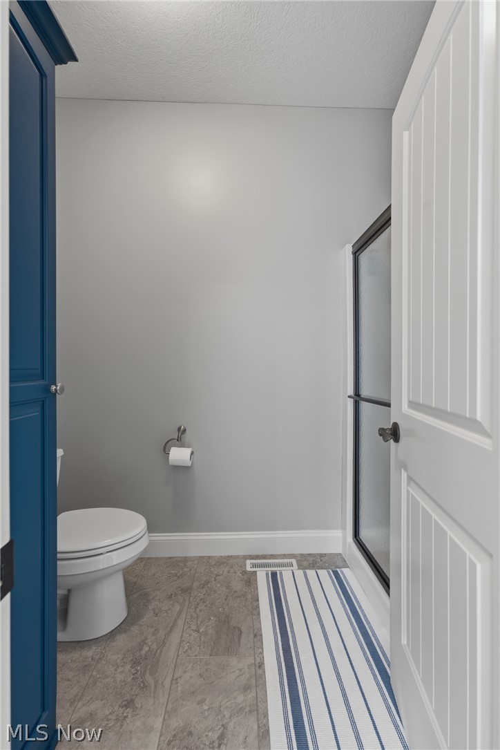 3955 Spring Brook Way Wooster, OH 44691 - Photo 17 of 50 Tile flooring, white toilet, glass shower enclosure with black framing, blue built-in cabinetry, and white panel door