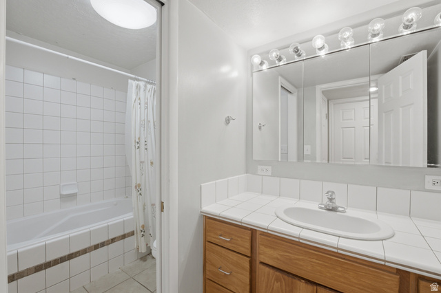 5788 Walden Ridge Drive Murray, UT 84123 - Photo 20 of 29 Bathroom featuring a built-in bathtub with white tile surround, a wood-finish vanity, a white tile countertop, and a mirrored medicine cabinet with overhead lighting