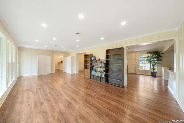 a view of an empty room with wooden floor and a kitchen