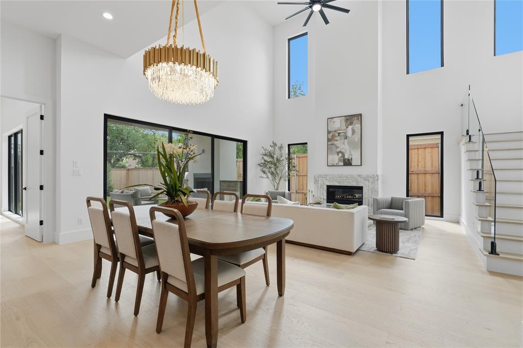 6038 Prospect Avenue Dallas, TX 75206 - Photo 13 of 40 Open-concept living space featuring wood-finish flooring, a contemporary chandelier, a fireplace with a stone surround, black-framed sliding glass doors, and a staircase with glass panel railing