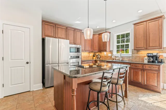 a kitchen with granite countertop a refrigerator a sink a stove a dining table and chairs