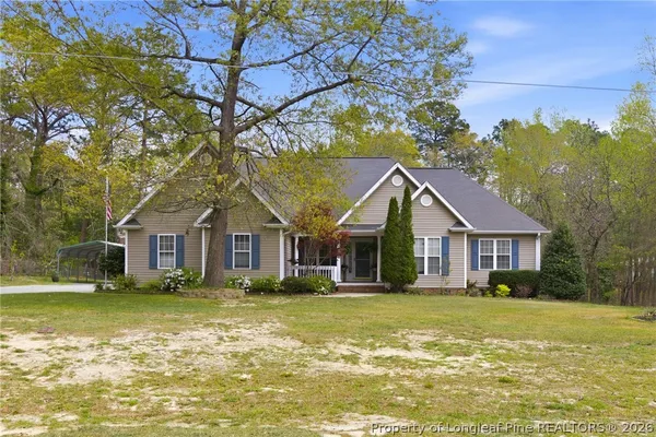 a view of a white house next to a yard with big trees
