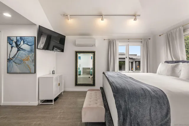 a spacious bedroom with a bed and a flat tv screen on the dresser