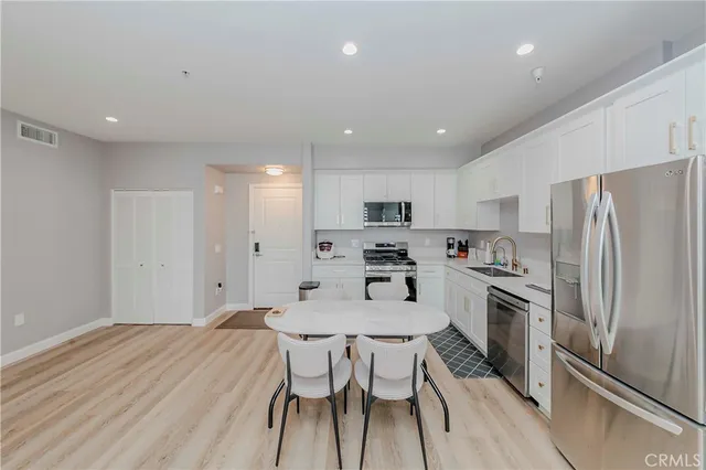 a kitchen with stainless steel appliances a refrigerator a stove a sink and white cabinets with wooden floor