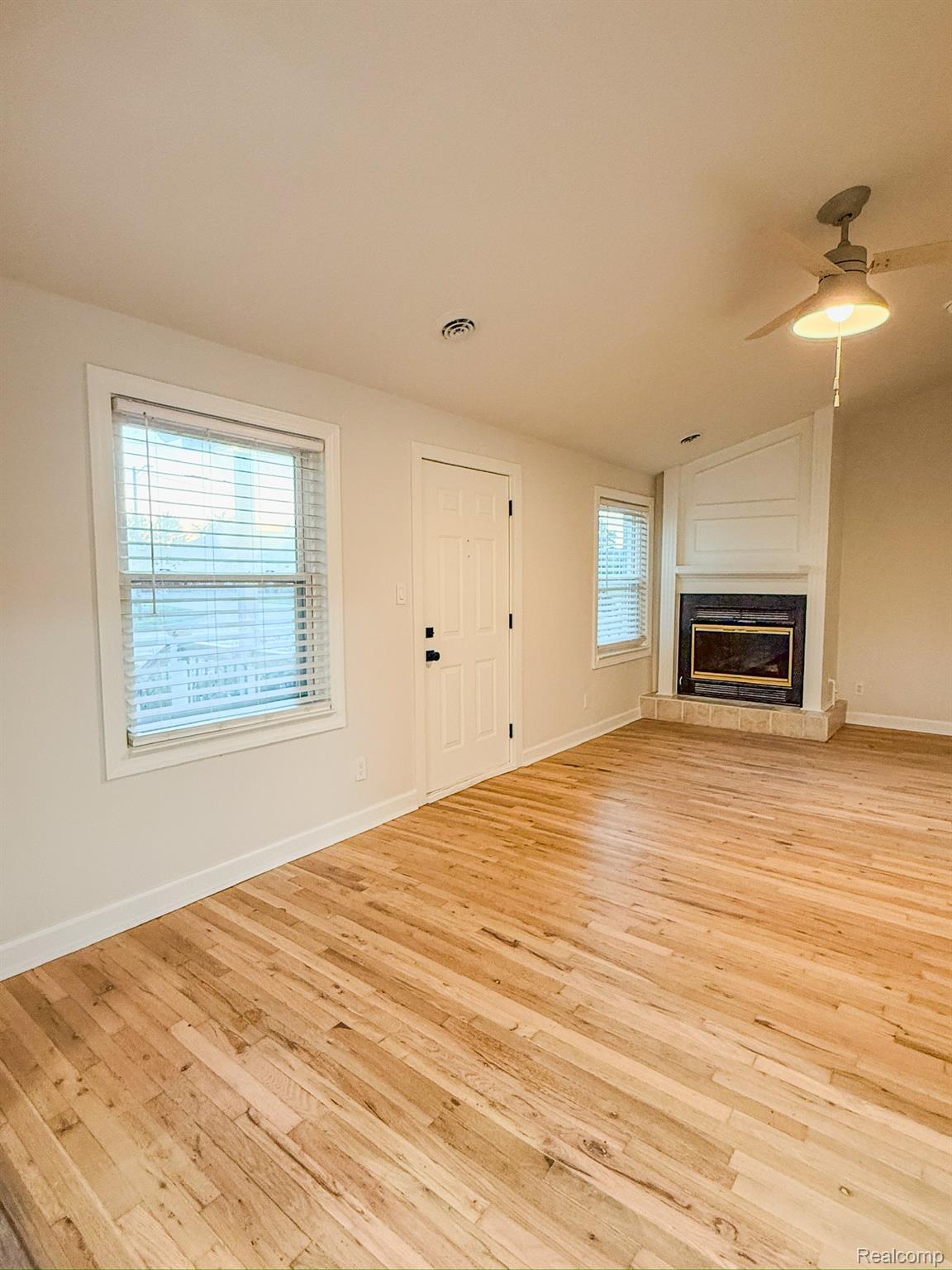 30052 Schoenherr Road Warren, MI 48088 - Photo 10 of 38 Bright living area featuring wood-finish flooring, a corner fireplace with a stone hearth, and white trim windows