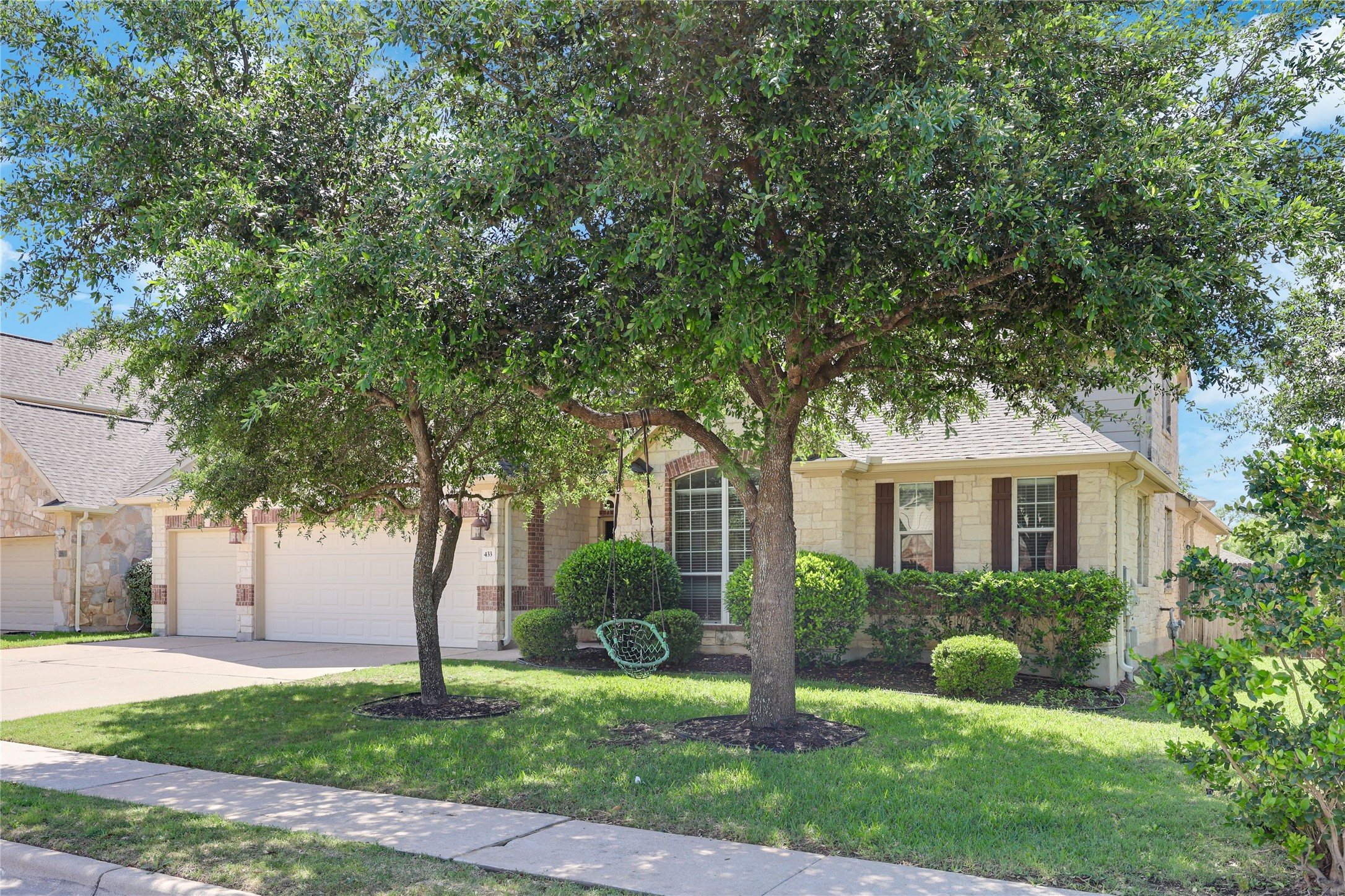 433 Ridgetop Bend Cedar Park, TX 78613 - Photo 2 of 34 View of property hidden behind natural elements with a front lawn, a garage, driveway, stone siding, and a shingled roof