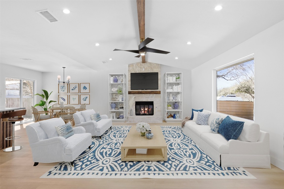 Living room featuring Minka Aire ceiling fan, brand new flooring, vaulted ceiling with a beam, and a stone fireplace