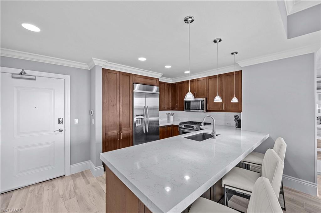 9115 Strada Place, Unit 5511 Naples, FL 34108 - Photo 7 of 38 a kitchen with stainless steel appliances granite countertop a sink a stove a refrigerator cabinets and a dining table with wooden floor