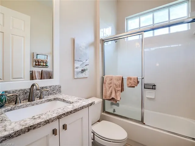 a bathroom with a granite countertop sink a mirror a toilet and shower