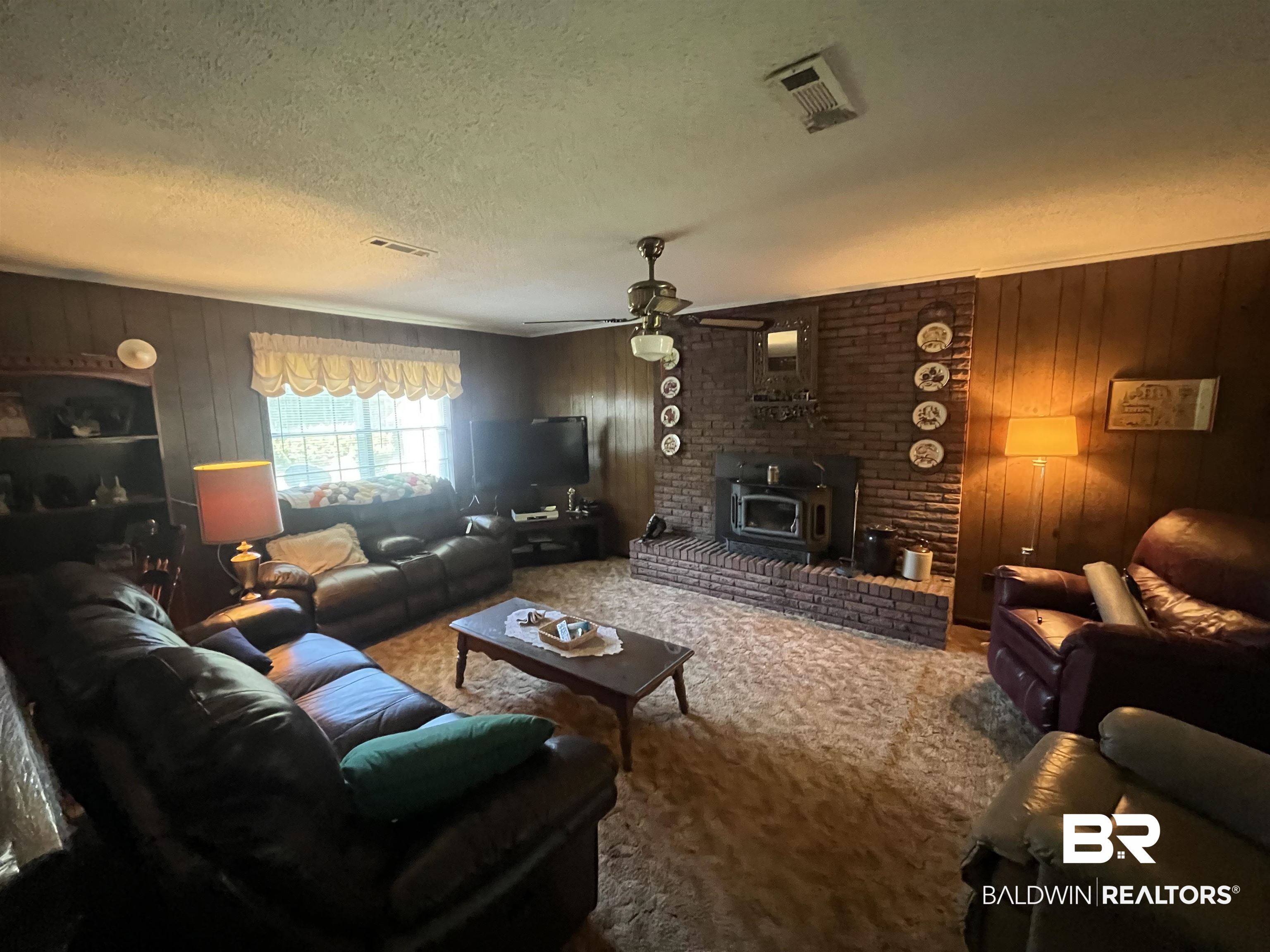 315 Dawkins Road Brewton, AL 36426 - Photo 12 of 19 Carpeted living room featuring a wood stove, a textured ceiling, visible vents, and wood walls
