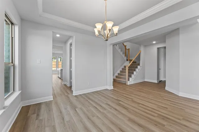 a view of an empty room with wooden floor stairs and a chandelier
