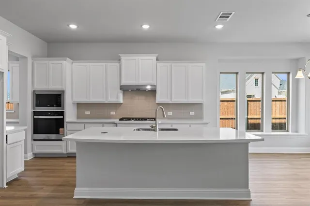 a large kitchen with stainless steel appliances granite countertop a stove a sink and a granite counter tops with wooden floors