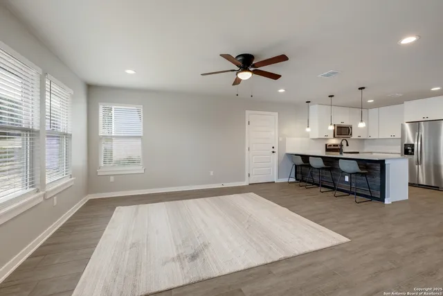 a living room with stainless steel appliances kitchen island granite countertop a stove a sink a refrigerator and white cabinets with wooden floor