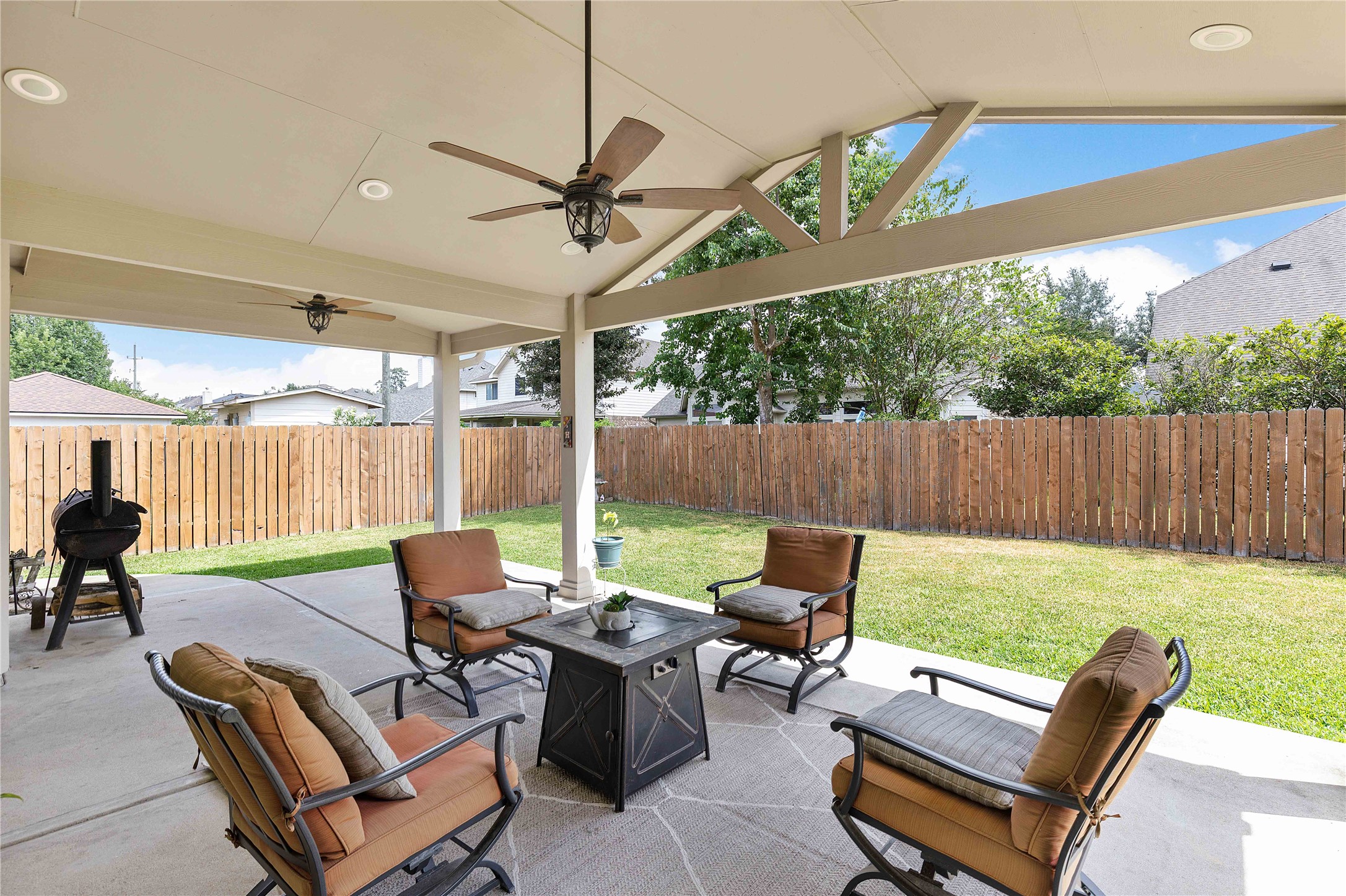 24506 Fort Path Drive Spring, TX 77373 - Photo 38 of 46 Spacious covered patio with ceiling fans, cozy seating, and a fire table, perfect for outdoor gatherings in a private fenced backyard.