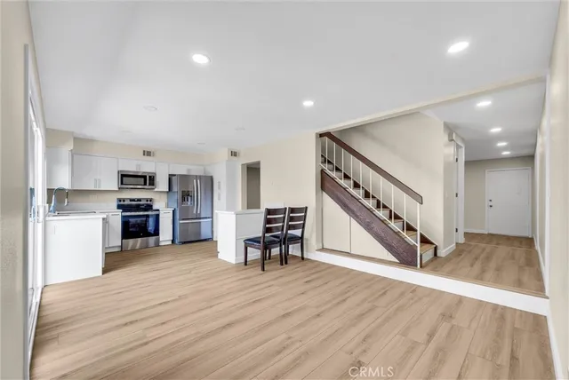 a kitchen with stainless steel appliances a stove top oven a sink a refrigerator a dining table and chairs with wooden floor