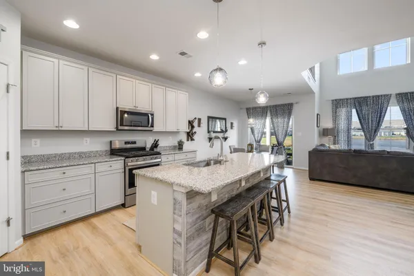 a kitchen with stainless steel appliances kitchen island granite countertop a stove a sink a refrigerator and white cabinets with wooden floor