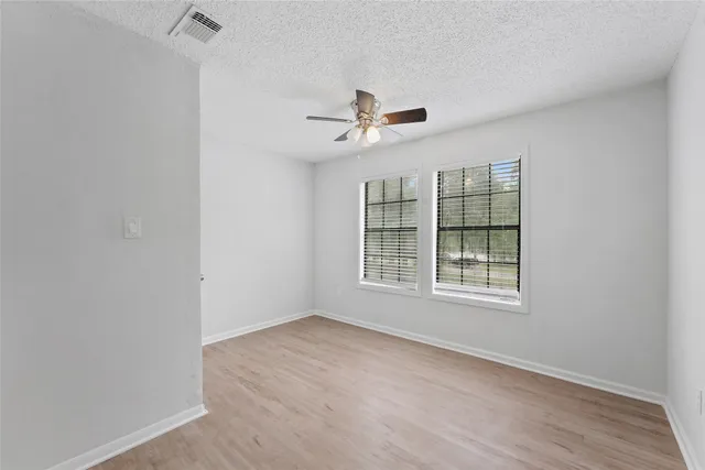 an empty room with wooden floor ceiling fan and windows