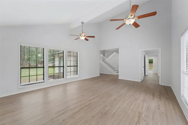 an empty room with wooden floor fan and windows