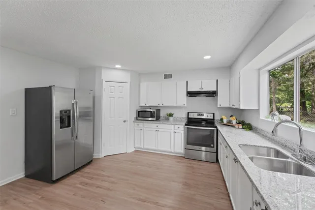 a large kitchen with a refrigerator a sink dishwasher a oven with white cabinets and wooden floor