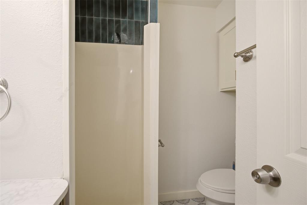 908 Isbell Road, Unit D Fort Worth, TX 76114 - Photo 17 of 27 Bathroom featuring a shower with dark teal subway tile, a white shower base, and a toilet with patterned floor tile