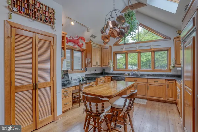 a kitchen with stainless steel appliances granite countertop a refrigerator a sink dishwasher a stove and a dining table with wooden floor