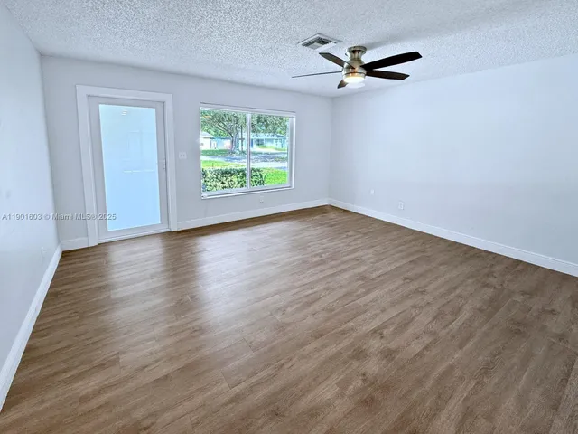 an empty room with wooden floor chandelier fan and windows