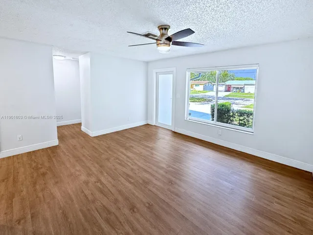 an empty room with wooden floor chandelier fan and windows
