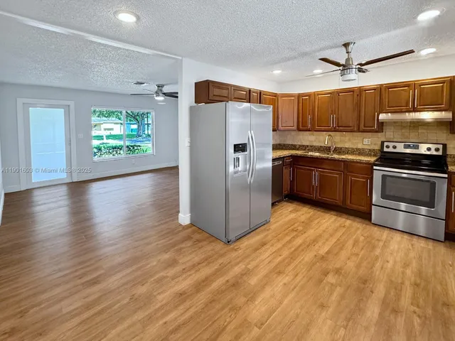 a kitchen with stainless steel appliances granite countertop a refrigerator a stove a sink and dishwasher with wooden floor
