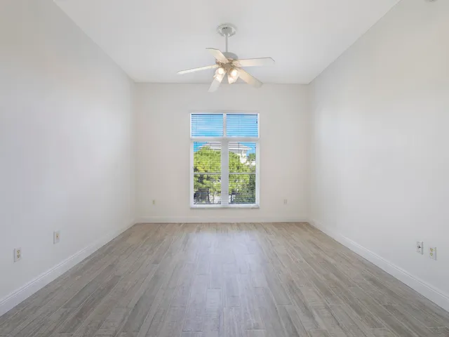 an empty room with wooden floor chandelier fan and windows
