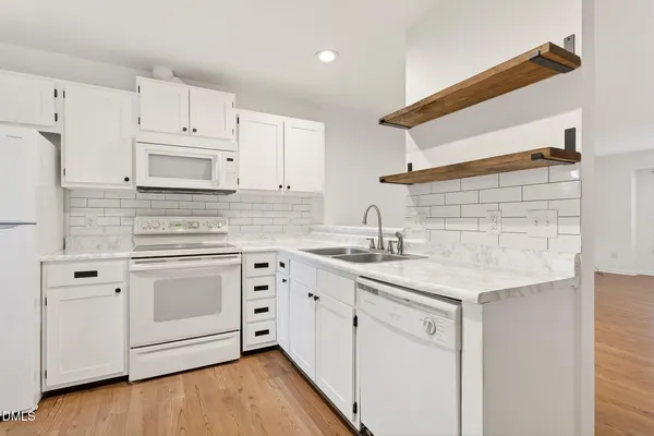 a kitchen with stainless steel appliances granite countertop white cabinets sink and white appliances