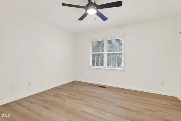 an empty room with wooden floor ceiling fan and window
