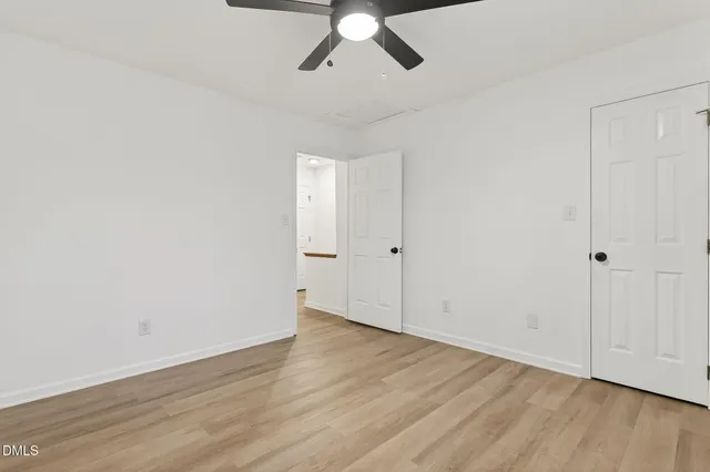 an empty room with wooden floor chandelier fan and windows