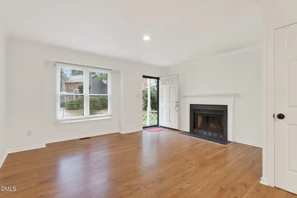 an empty room with wooden floor fireplace and windows