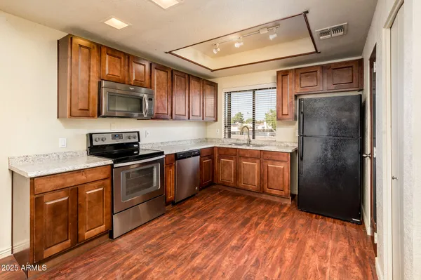 a kitchen with stainless steel appliances granite countertop a refrigerator a sink dishwasher a stove with wooden cabinets and floor