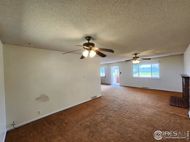 an empty room with chandelier fan and windows