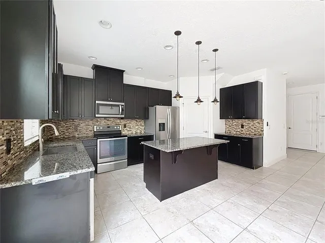 a large kitchen with kitchen island granite countertop a sink a counter top space and cabinets