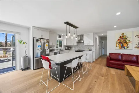 a kitchen with stainless steel appliances kitchen island granite countertop a refrigerator a stove top oven a dining table and chairs with wooden floor